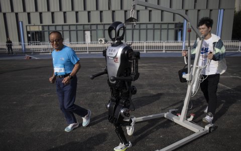 Zhang Xianhua (71 años), un corredor que participará en la carrera, trota junto a un robot humanoide antes de una carrera entre humanos y robots en Pekín.