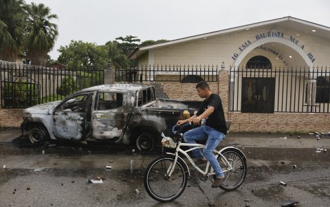 Una persona transita frente a un vehículo quemado durante una jornada de manifestaciones.
