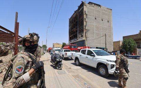 Las fuerzas de seguridad bloquean la carretera frente a un edificio carbonizado después de que un incendio arrasara el recién inaugurado Hyper Mall en la ciudad de Kut.