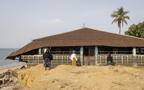 Los residentes se encuentran junto a una sección de una mezquita que se derrumbó debido a los efectos del aumento del nivel del mar en la isla Plantain.