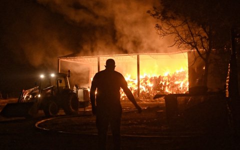 Bomberos y voluntarios combatieron un almacén en llamas durante un incendio forestal en la aldea de Feneos, municipio de Corinto, Grecia, este miércoles 23 de julio.