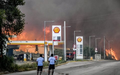 Los habitantes se encuentran en una carretera mientras un incendio forestal se acerca a una gasolinera cerca de la ciudad de Patras, en el oeste de Grecia, el 12 de agosto de 2025.