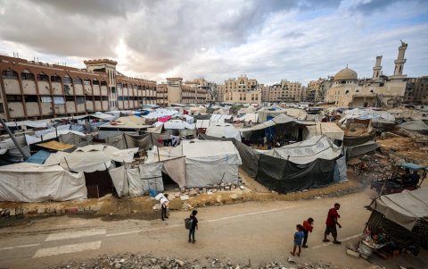 Un hombre y niños caminan junto a tiendas de campaña que albergan a personas desplazadas por la guerra, instaladas cerca de la mezquita Sheikh Hamad bin Khalifa Al-Thani, gravemente dañada.