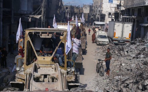 Las excavadoras pasan junto a los palestinos en un camino de tierra, en el camino para limpiar los escombros de los edificios y calles principales de la ciudad de Gaza.