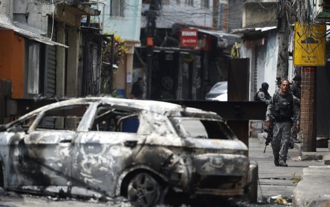 Un integrante de la Policía de Río de Janeiro camina junto a un vehículo incinerado este martes, en Río de Janeiro (Brasil).