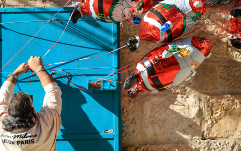 Un palestino coloca globos navideños a las puertas de su negocio durante el tradicional desfile de Navidad por las calles de Belén.
