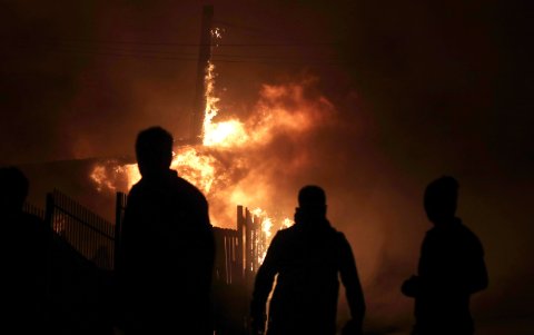 Personas observan viviendas afectadas por los incendios forestales.