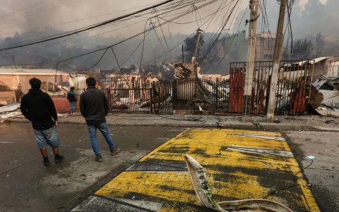 Varias personas observan casas afectadas tras incendios forestales este domingo, en la comuna de Penco, Concepción (Chile).