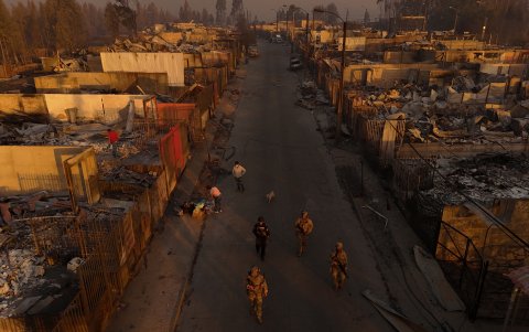 Vista aérea, soldados patrullan una calle bordeada de restos carbonizados de casas destruidas al atardecer después de un incendio forestal en Concepción, Chile.