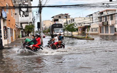 Motociclistas atraviesan calles inundadas en Machala, donde el estancamiento de agua ha limitado el acceso a locales y reducido la actividad comercial.