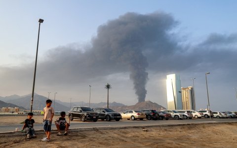 Unos niños sentados al costado de carretera observan cómo se eleva una alta columna de humo tras una explosión en la zona industrial de Fujairah (Emiratos Árabes Unidos).