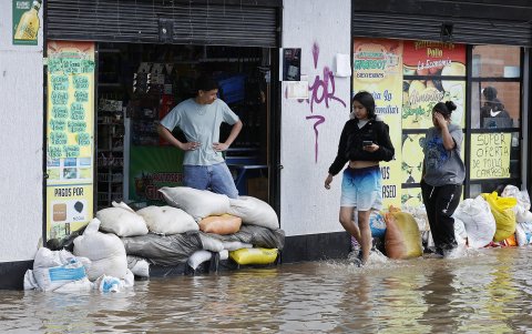 Personas usan sacos de arena para impedir que el agua entre a las casas debido a las inundaciones por fuertes lluvias este jueves, en Facatativá (Colombia).