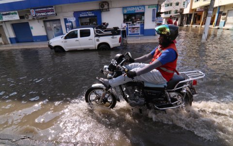 Un motociclista levanta los pies para no mojarse a causa de los estragos de la inundación en  las calles de Milagro