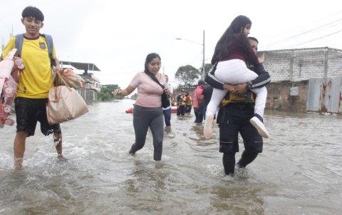 Padres llevando a niños en brazos fue una escena peculiar en Milagro, afectada por las inundaciones.