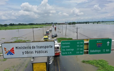 La vía Babahoyo–Jujan permanece inundada, mientras personas ayudan a guiar a los conductores para evitar huecos en la carretera.