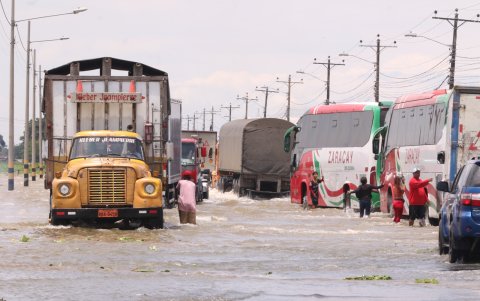 La inundación de la vía ha generado una forma improvisada de sustento: algunas personas ayudan a conductores a recuperar las placas perdidas por el agua.