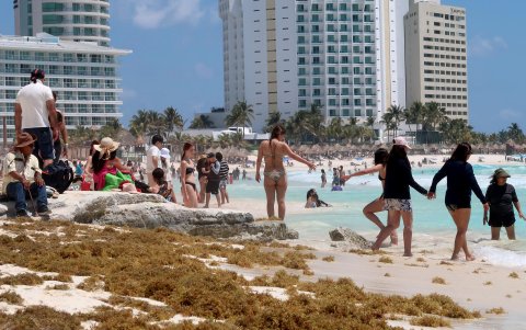 Turistas caminan en una playa impactada por el sargazo este lunes en el balneario de Cancún en Quintana Roo (México).
