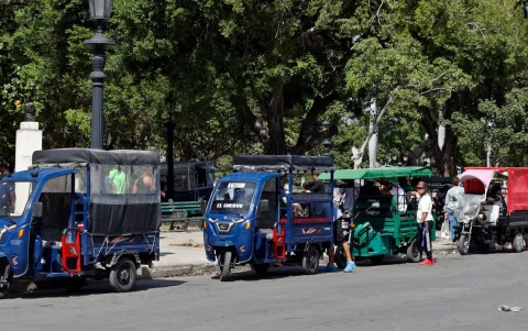 Personas a bordo de triciclos eléctricos utilizados como taxis esperan la llegada de clientes en una calle este martes, en La Habana (Cuba).
