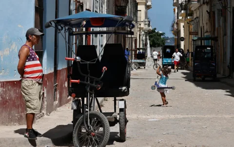 Una persona con una camiseta de la bandera de los Estados Unidos espera junto a un bicitaxi, en La Habana, (Cuba).