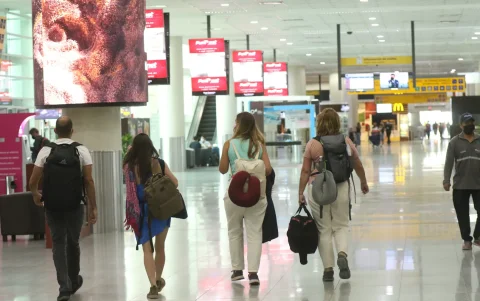 Personal aeroportuario y viajeros se movilizan hacia la terminal aérea con documentación de vuelo en medio de las restricciones nocturnas.