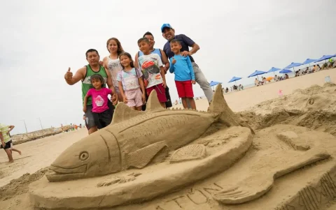 Un grupo de turistas se toma una foto frente a una escultura hecha con arena en una playa de Manabí.