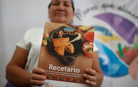 Una mujer sostiene un recetario del proyecto de seguridad alimentaria Manos que Alimentan.