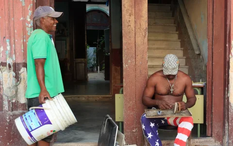 Fotografía de un zapatero arreglando calzado y hablando con otra persona en una calle de La Habana (Cuba).