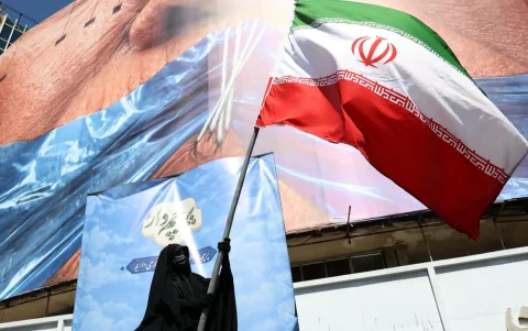 Una mujer con velo sostiene la bandera nacional de Irán frente a una enorme valla publicitaria antiestadounidense en Teherán, Irán, el 11 de mayo de 2026.