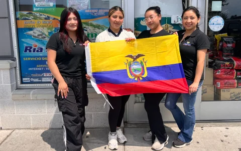 Trabajadoras latinas posan con orgullo sosteniendo la bandera de Ecuador frente a los escaparates de un supermercado local en el área de Filadelfia.