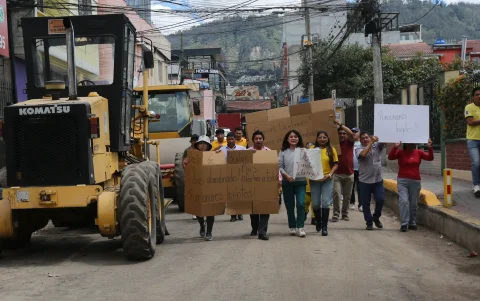 Maquinaria detenida en la vía sin trabajadores visibles, mientras moradores de Cumbayá realizan una marcha de protesta por obras inconclusas.