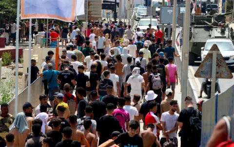 Inmigrantes caminan por una vía en Ceuta, bajo vigilancia de vehículos militares.