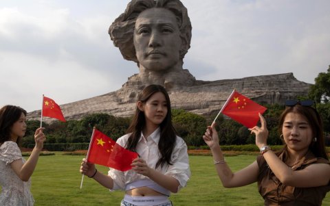 Unas mujeres sostienen banderas chinas junto a la escultura del joven Mao Zedong en Changsha, provincia de Hunan, China, el 9 de septiembre de 2026.