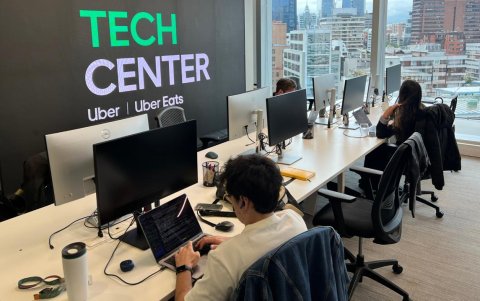 Profesionales del Uber Tech Center Santiago en sus puestos de trabajo, con la cordillera de los Andes al fondo, en la Gran Torre Santiago.