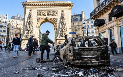 La gente pasa junto a un coche calcinado tras los enfrentamientos entre la policía antidisturbios y los manifestantes en París.
