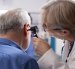 Experienced retired female physician inspecting ear of elderly male patient in clinic office. Closeup of skilled old doctor using otoscope during medical consultation of senior white man.