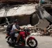 Personas transitan en motocicleta frente a edificios colapsados por los terremotos en Catia La Mar, Venezuela.