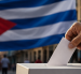 Una persona deposita su voto en una urna, con la bandera de Cuba de fondo, en una representación sobre el debate en torno al sistema electoral de la isla.