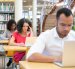 Diverse adult students working on computer in classroom. Focused sitting at desks and using laptops. Bookshelves in background. Education concept