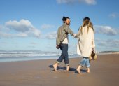 Side view of Caucasian couple on summer vacation. Bearded man and woman in casual clothes walking on beach, holding hands. Love, travelling, tenderness concept