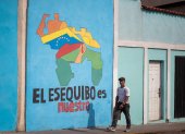 Transeúntes caminando frente a un mural con el mapa de Venezuela que dice "El Esequibo es nuestro", en Caracas.