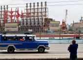 Un auto viejo de transporte colectivo al pasar frente a una planta flotante de generación eléctrica en el puerto de La Habana (Cuba).