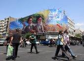 Iraníes pasan frente a una gran valla publicitaria con los difuntos líderes supremos iraníes, los ayatolás Ruhollah Jomeini y Ali Jameneí, en una calle de Teherán, Irán.