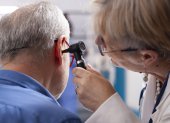 Experienced retired female physician inspecting ear of elderly male patient in clinic office. Closeup of skilled old doctor using otoscope during medical consultation of senior white man.