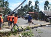 Trabajadores retiran un árbol caído y un pilón eléctrico (L) destruido a la altura del tifón Phanfone en la ciudad de Salcedo, provincia de Samar Oriental, este 26 de diciembre.