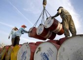Un grupo de trabajadores mueven barriles con petróleo.