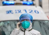 Referencial. Una enfermera totalmente protegida atiende una llamada telefónica junto a su ambulancia en Wuhan.