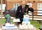 A handout picture released on April 30, 2020 shows Captain Tom Moore posing for a photograph with cakes to celebrate his 100th birthday in Marston Moretaine, north of London. (Photo by Emma SOHL / CAPTURE THE LIGHT / AFP) / RESTRICTED TO EDITORIAL USE - MANDATORY CREDIT "AFP PHOTO / CAPTURE THE LIGHT / EMMA SOHL" - NO MARKETING NO ADVERTISING CAMPAIGNS - DISTRIBUTED AS A SERVICE TO CLIENTS --- NO ARCHIVE ---