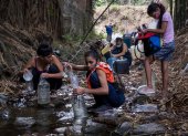 Cientos de ciudadanos recogen agua de un riachuelo.