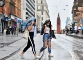 Two women wearing protective face masks cross tram tracks in the rain in Birmingham, central England on August 22, 2020, as Britain"s second-city, home to more than one million people, was made an "area of enhanced support", because of concern about a spike in cases of the novel coronavirus. (Photo by JUSTIN TALLIS / AFP)