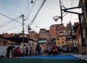 Un grupo de niños y jóvenes juega baloncesto para inaugurar una recién restaurada cancha improvisada por los vecinos del barrio.